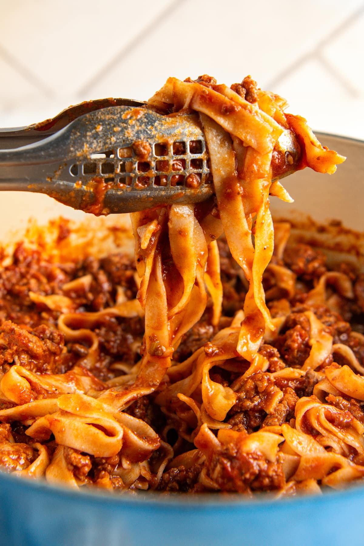 Using tongs to serve a portion of pasta with ragu spaghetti sauce.