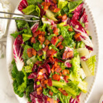 Wilted lettuce salad with hot bacon dressing on a white serving plate.