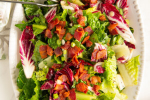 Wilted lettuce salad with hot bacon dressing on a white serving plate.