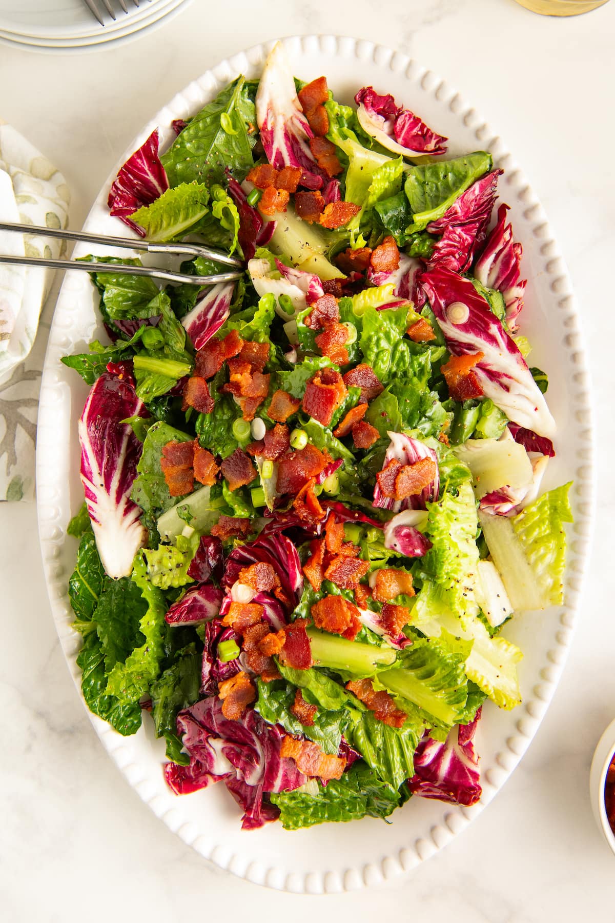 Wilted lettuce salad with hot bacon dressing on a white serving plate.