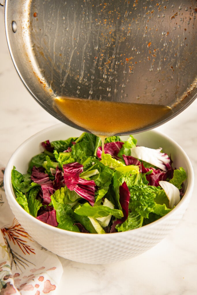 Pouring hot bacon dressing over mixed salad greens.