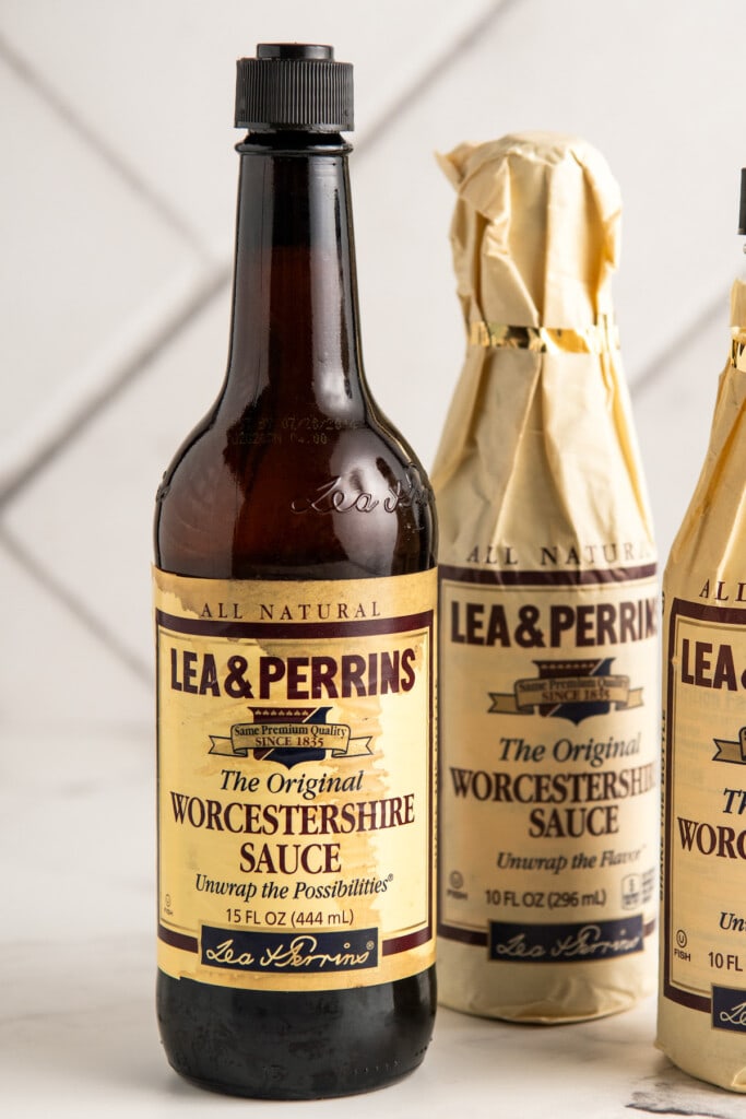 Three bottles of Worcestershire sauce arranged on a marble countertop.