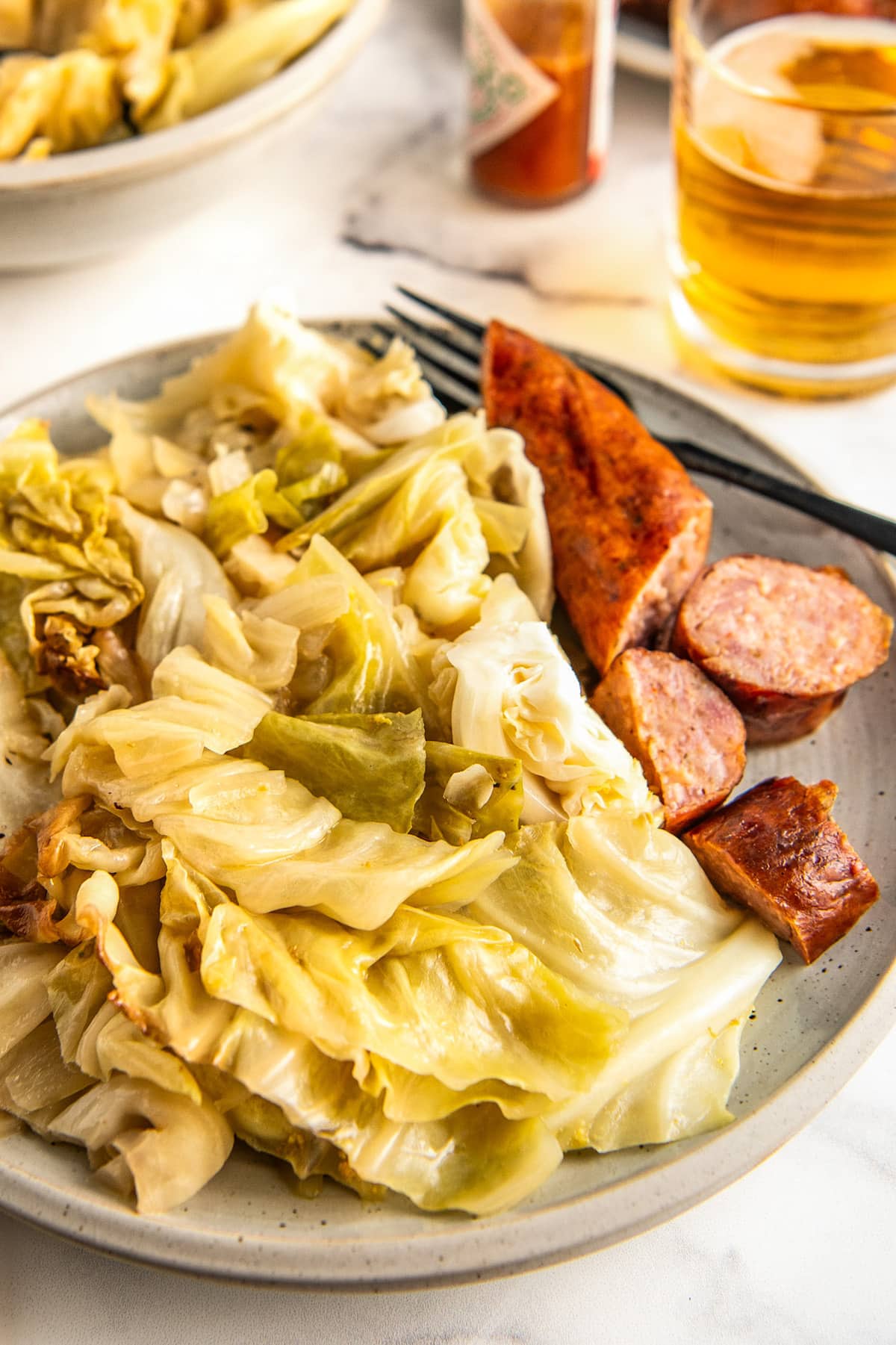Buttery and tender crockpot cabbage served on a plate next to a side of sliced sausage. 