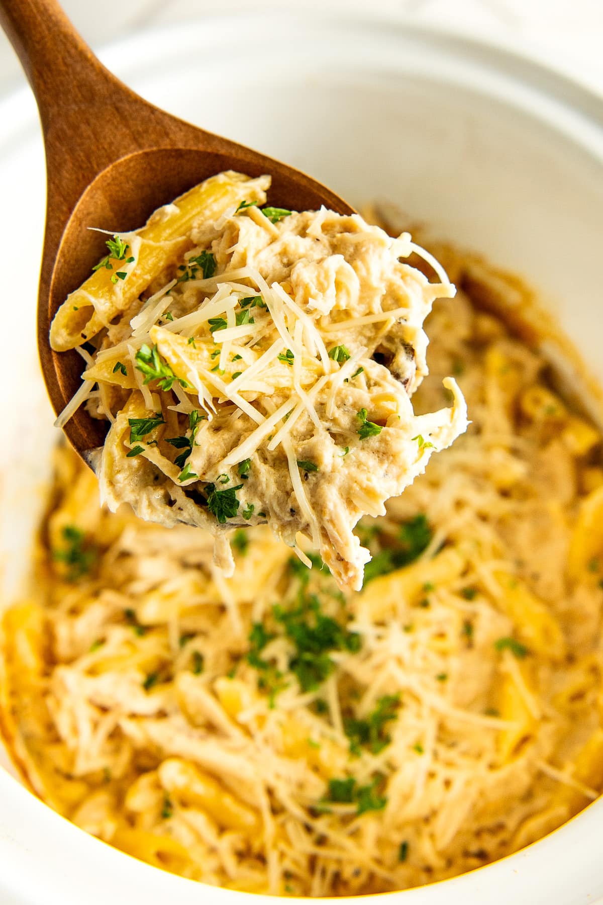 Close up of a wooden spoon of crockpot chicken Alfredo being scooped out of a slow cooker. 