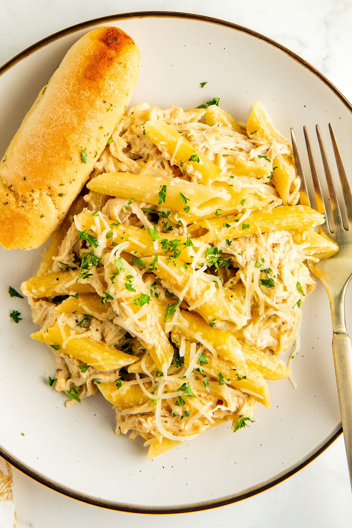 A plate of chicken Alfredo with a fork and one garlic breadstick on the side.