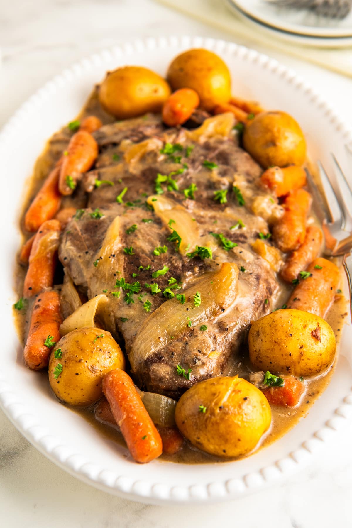 A serving platter filled with juicy and tender London broil slow cooked in a rich gravy with potatoes, onions and carrots.