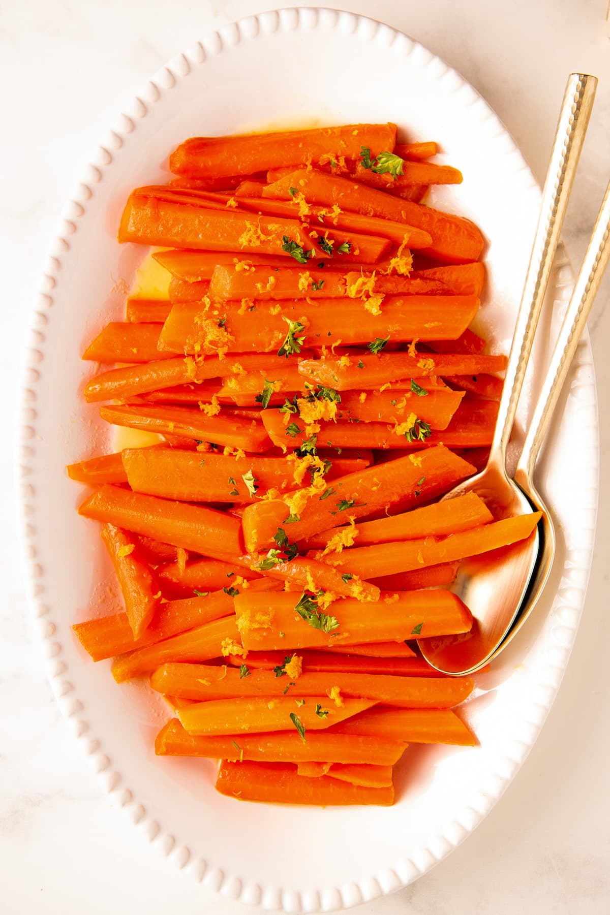 Honey glazed carrots on a white serving plate topped with fresh herbs and orange zest.