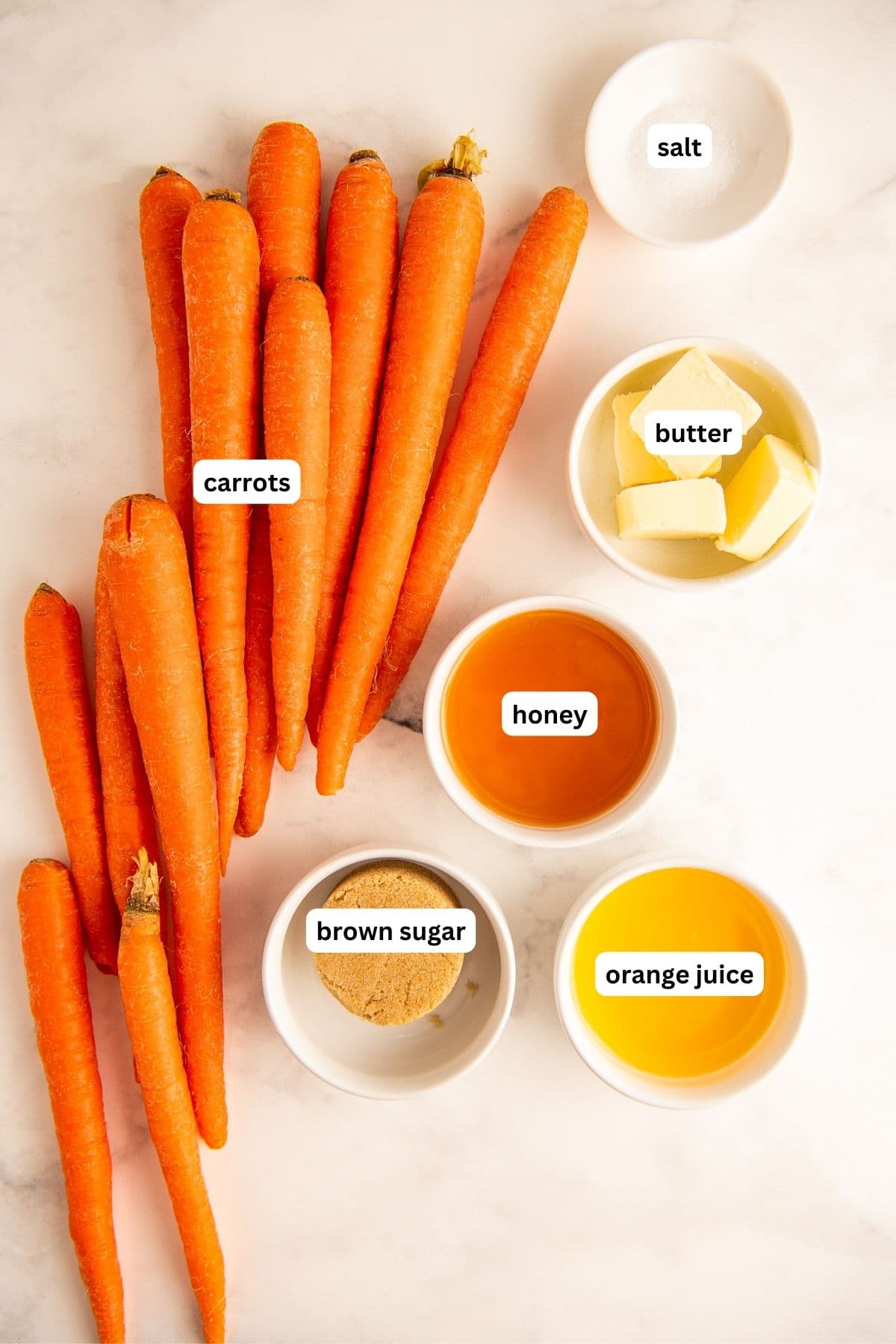 Ingredients arranged in bowls to make honey glazed carrots recipe. From top to bottom: salt, carrots, butter, honey, brown sugar and orange juice.
