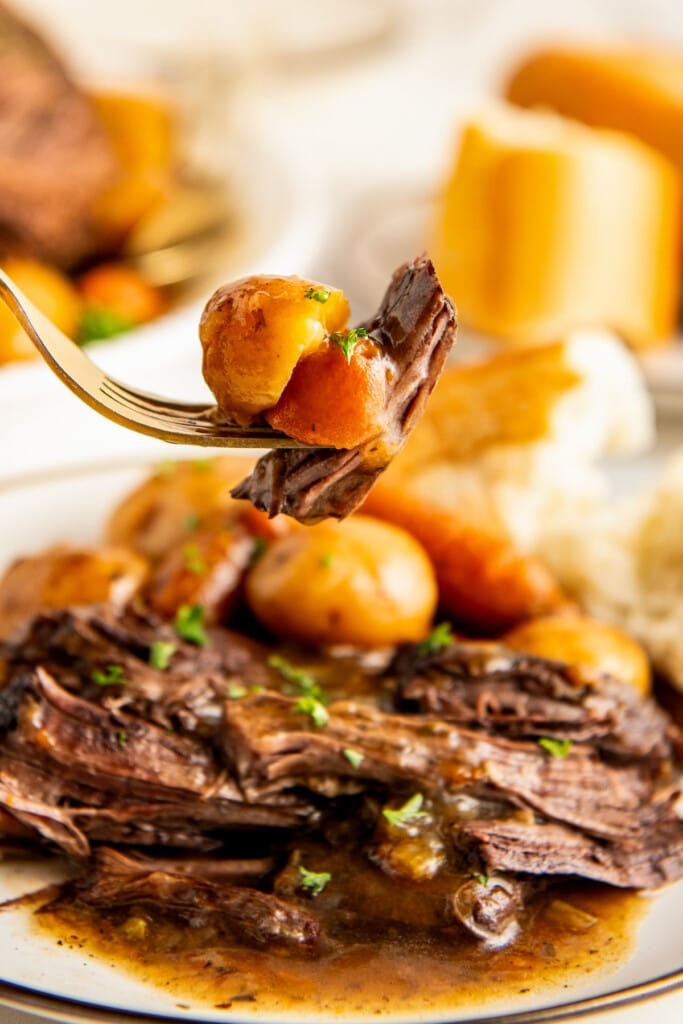 Taking a big bite of roast beef with potato and carrot.