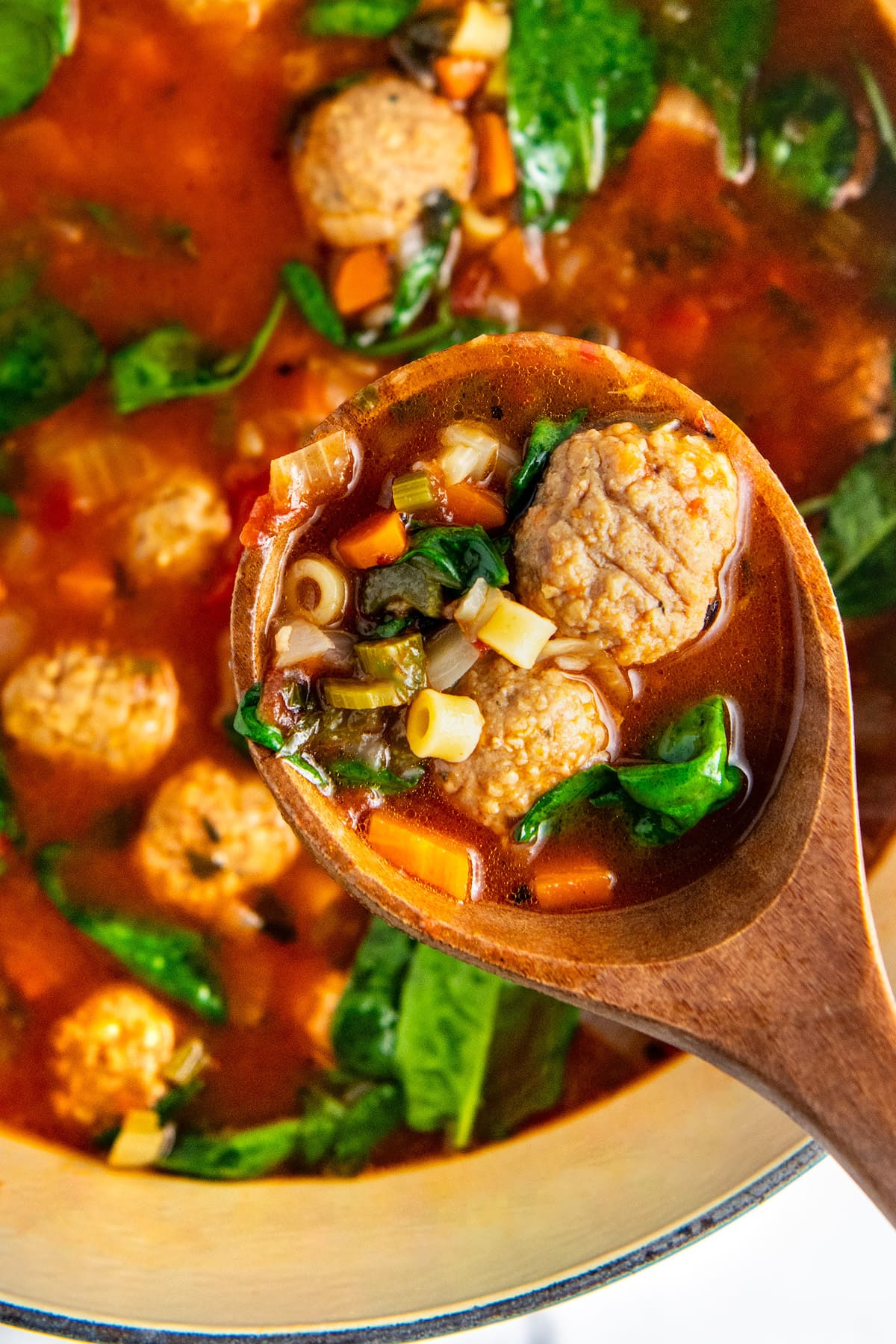 A wooden spoon serving Italian meatball soup out of the pan.