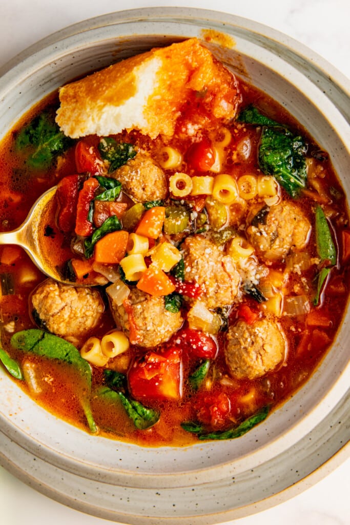 A spoon in a bowl of Italian meatball soup topped with grated parmesan cheese. 