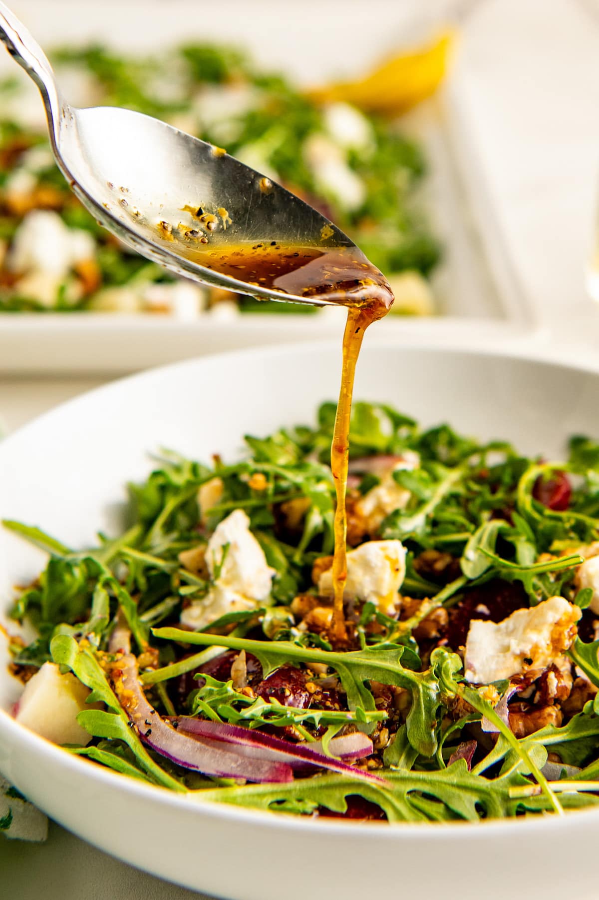 Drizzling homemade salad dressing over a fresh arugula salad with a spoon.