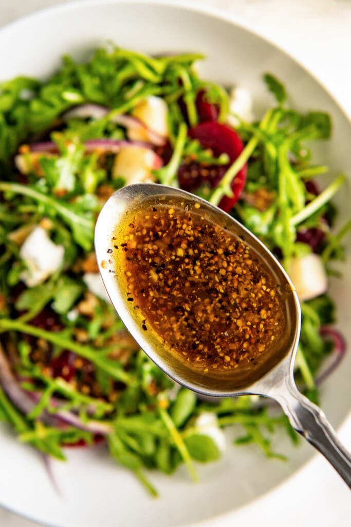 Adding lemon balsamic dressing on top of the salad with a spoon.