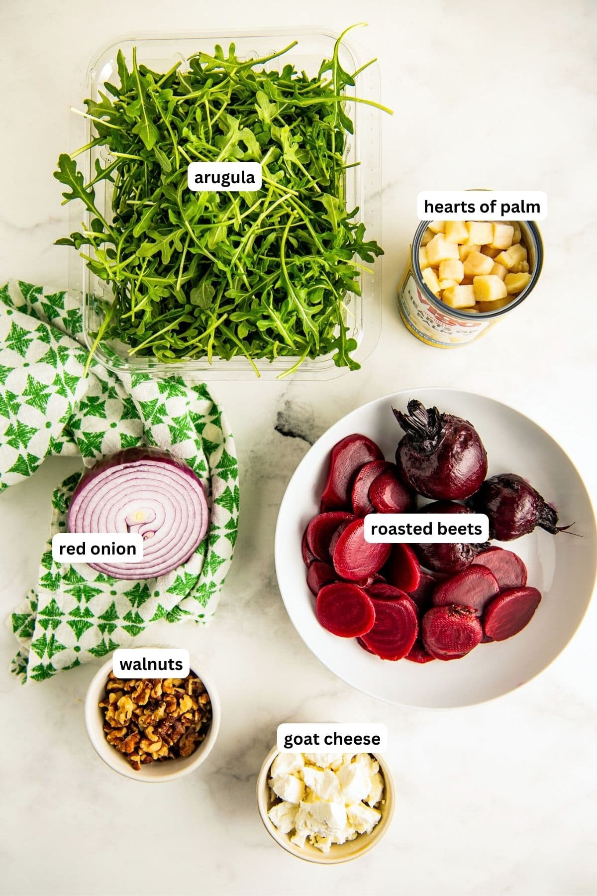 Ingredients for roasted beet salad recipe arranged in bowls, from top to bottom: arugula, hearts of palm, red onion, roasted beets, walnuts and crumbled goat cheese. 