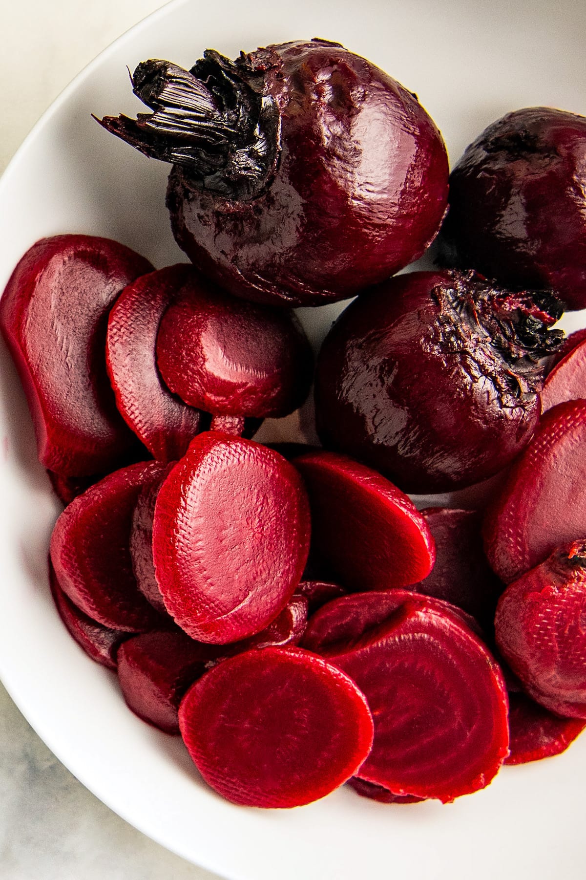 A white plate with whole and sliced roasted beets.