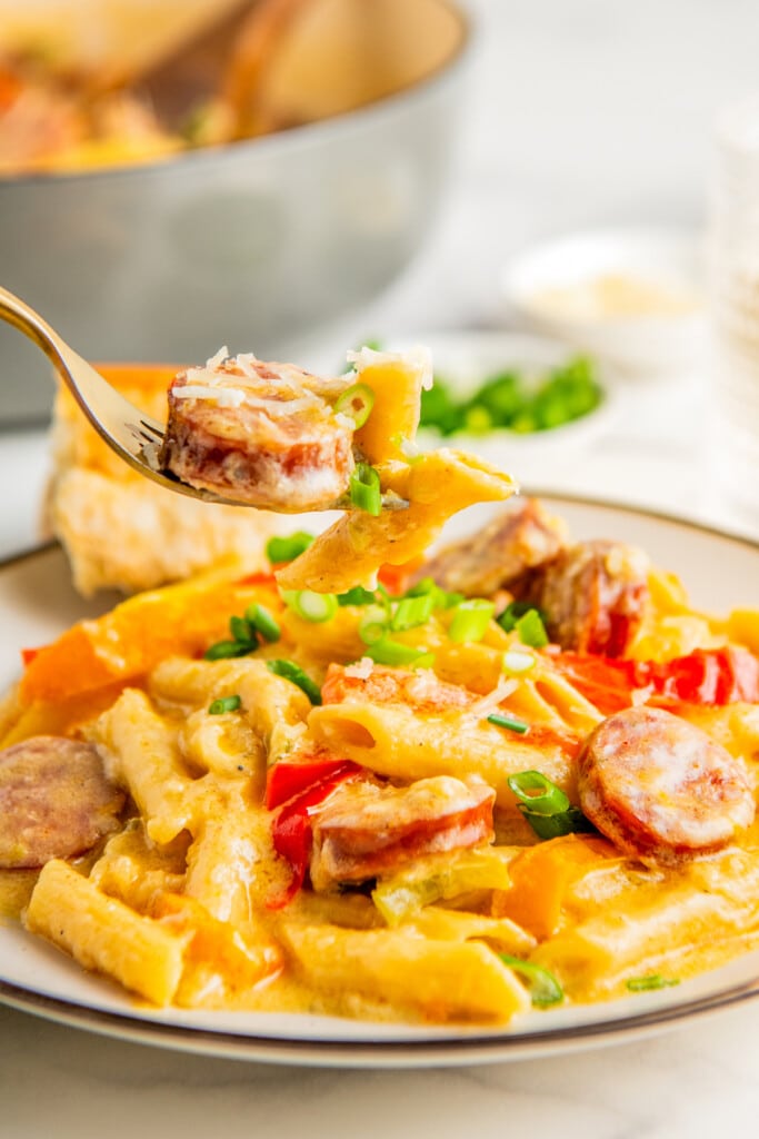 A fork taking a bite of creamy cajun pasta with sausage off a plate.
