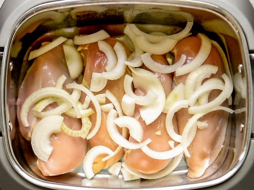 Chicken breasts in a crockpot with sliced onions on top.