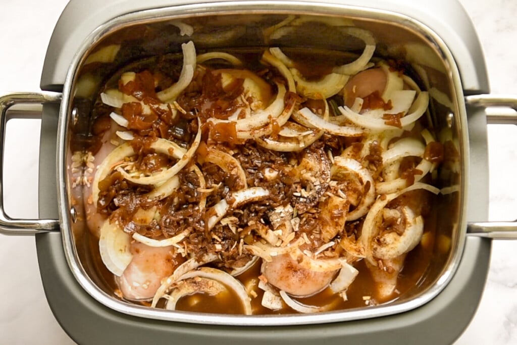 Chicken and french onion soup in crock pot topped with sliced onions and seasonings before cooking.
