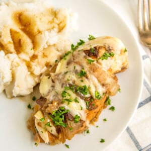 A piece of crockpot french onion chicken topped with melted cheese and fresh herbs next to a side of mashed potatoes.