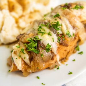 Juicy and tender crockpot french onion chicken topped with melty cheese on a plate with a side of mashed potatoes.