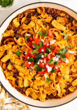 Overhead shot of Frito pie garnished with tomato, onion, and jalepeno.