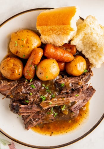 Juicy and tender instant pot roast with potatoes and carrots in a rich and savory beef gravy on a plate with a side of crusty bread.