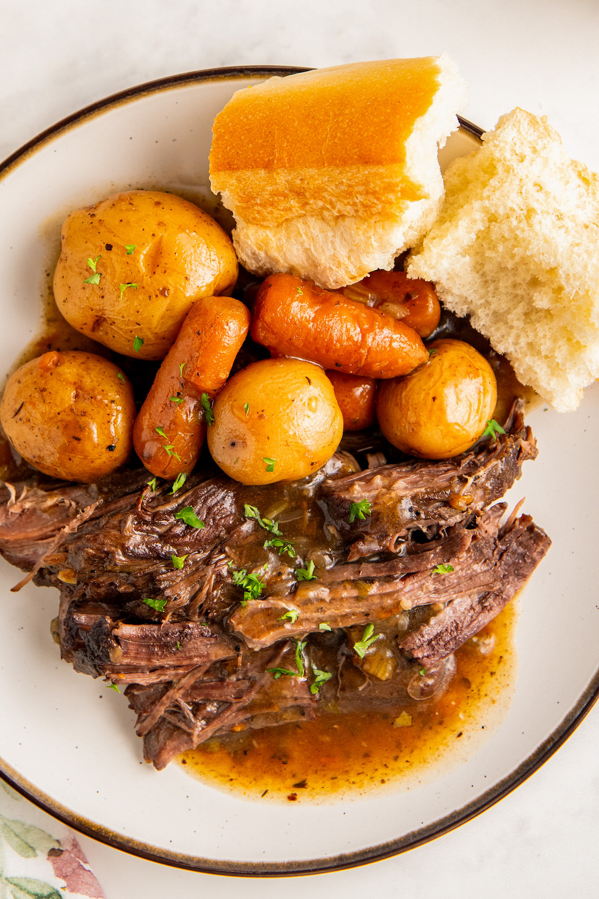Juicy and tender instant pot roast with potatoes and carrots in a rich and savory beef gravy on a plate with a side of crusty bread.
