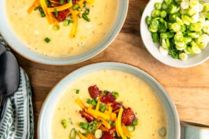 2 bowls of potato soup on a wooden serving board.