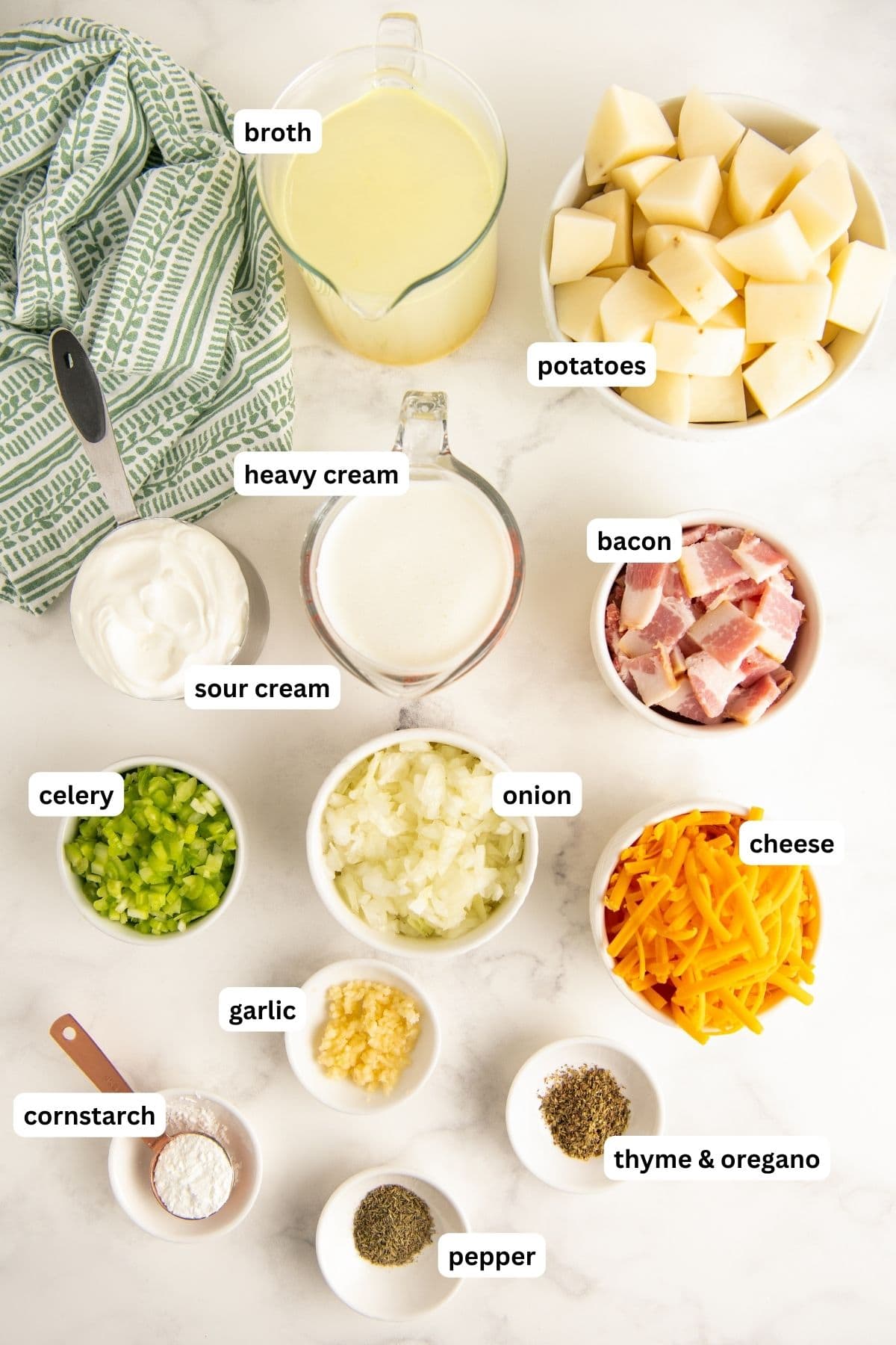 Ingredients to make instant pot potato soup recipe, arranged in bowls. From top to bottom: chicken broth, potatoes, heavy cream, sour cream, bacon, celery, onion, garlic, cheddar cheese, cornstarch, thyme, oregano, salt and pepper.