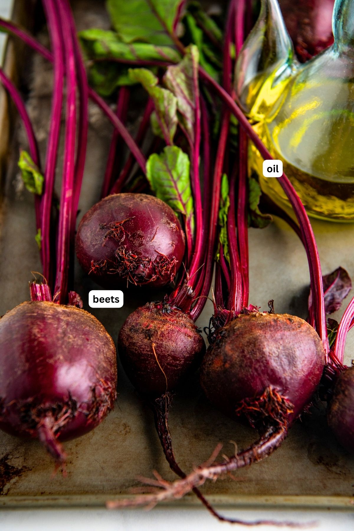 Whole beets on a cookie sheet with a bottle of olive oil on the side.