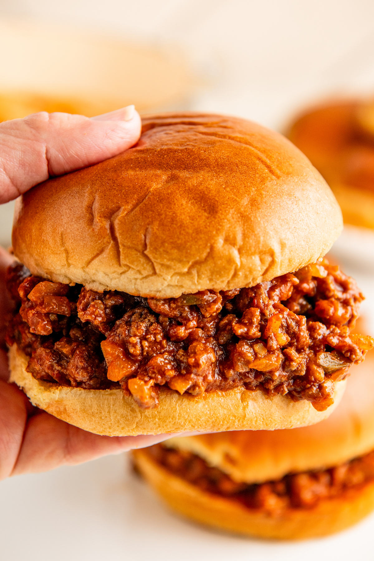 A hand holding an easy sloppy Joe on a toasted bun getting ready to take a bite.