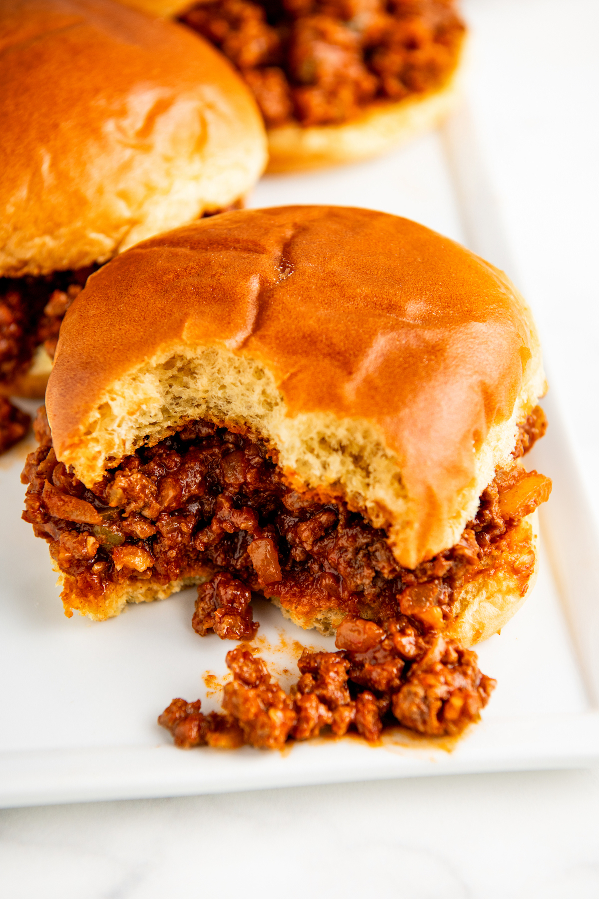 A bite missing from a homemade sloppy Joe sandwich on a plate.