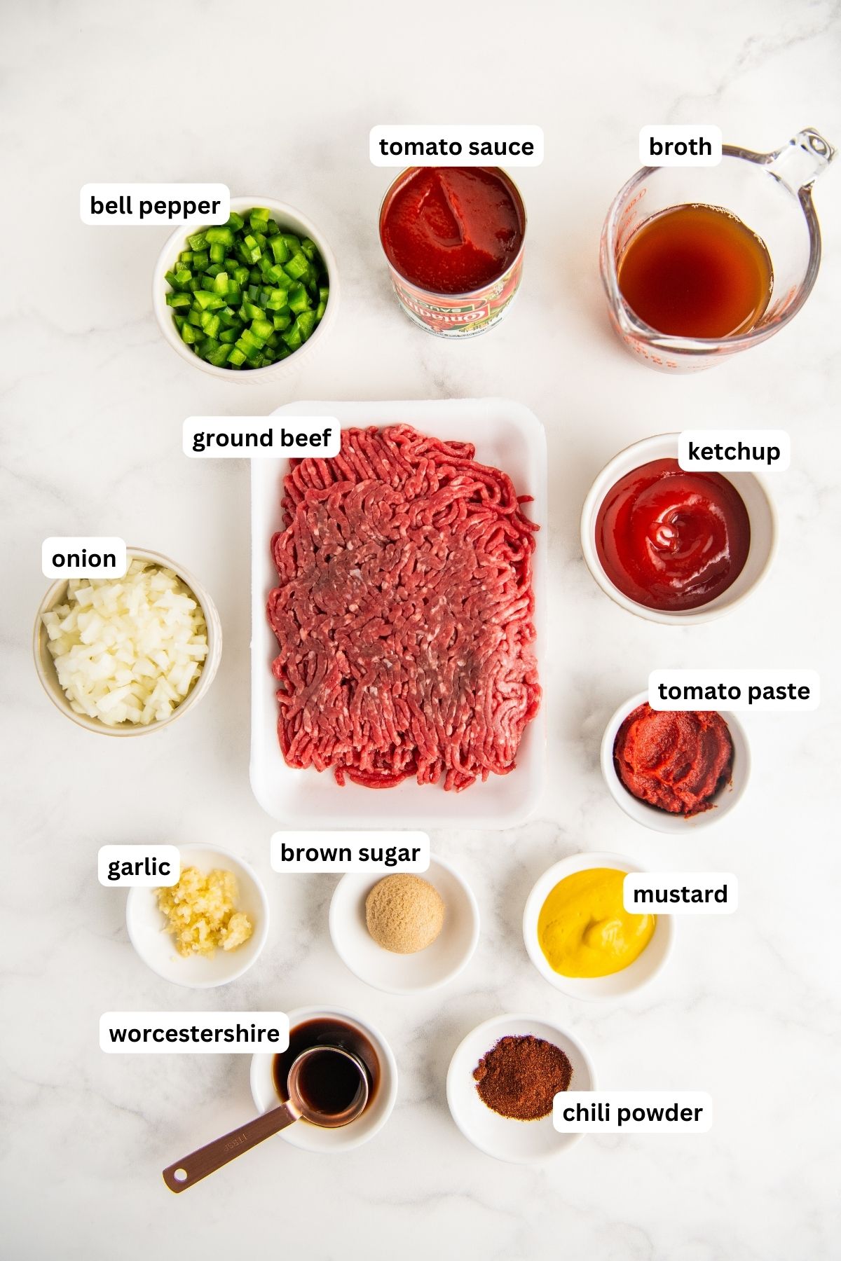 Ingredients to make homemade sloppy Joes arranged in bowls, from top to bottom: tomato sauce, broth, bell pepper, ground beef, ketchup, onion, tomato paste, garlic, brown sugar, mustard, Worcestershire sauce and chili powder. 