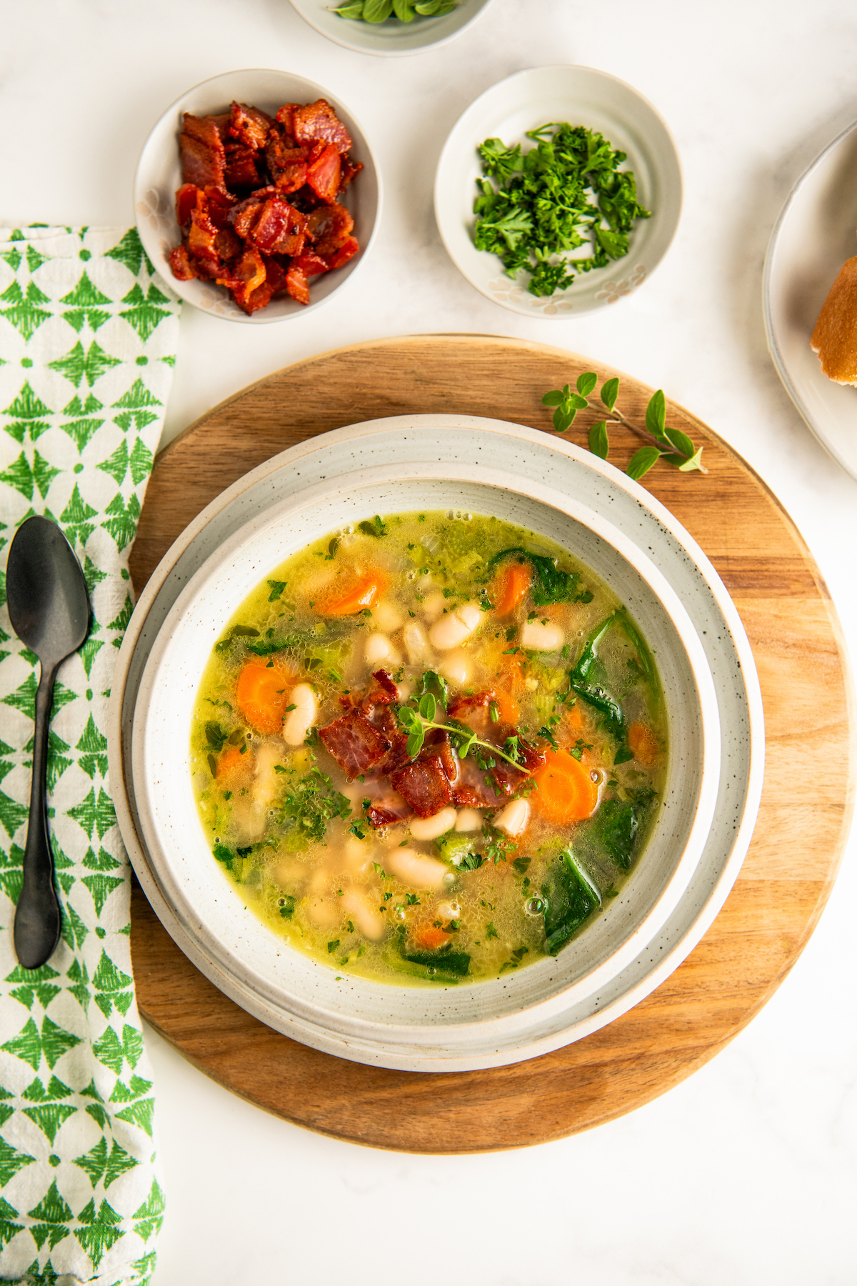 A bowl of tender white bean and bacon soup garnished with crispy bacon and fresh herbs on top.