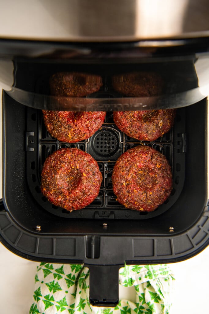 Four uncooked burgers in air fryer basket.