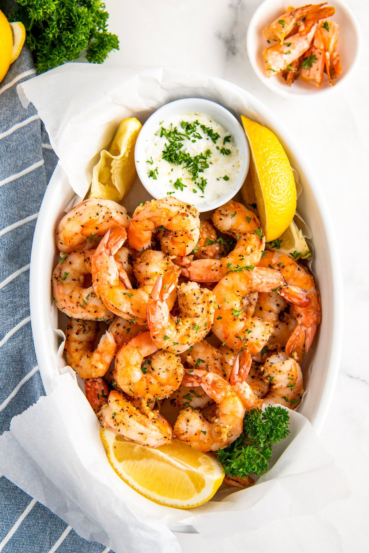 Tender and juicy air fryer shrimp with garlic and lemon wedges and a bowl of discarded shrimp tails on the side.