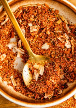 A golden spoon resting in a bowl of burger seasoning.