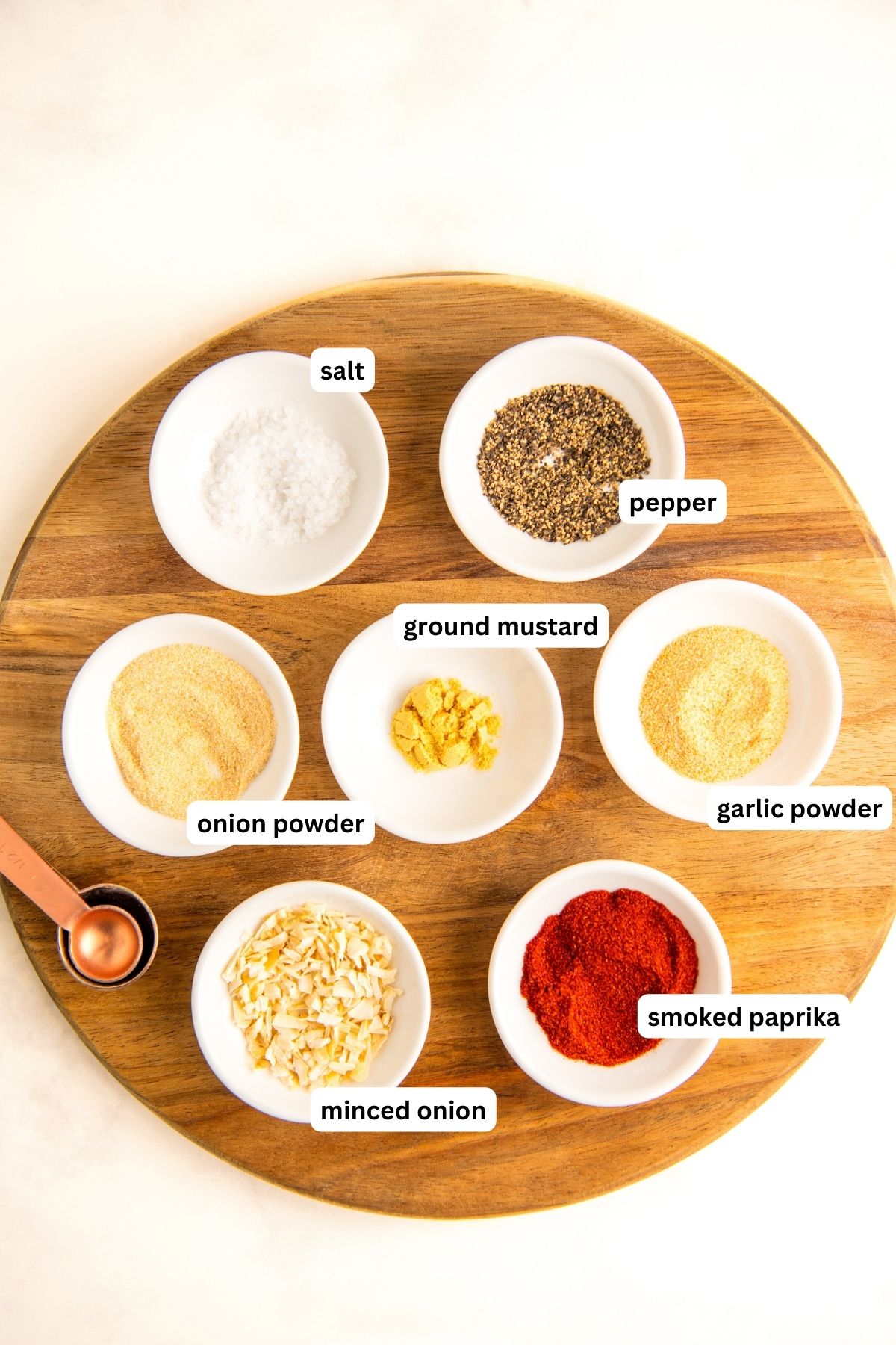 Ingredients needed for homemade burger seasoning recipe arranged in bowls. From top to bottom: salt, pepper, onion powder, ground mustard, garlic powder, onion flakes and smoked paprika. 