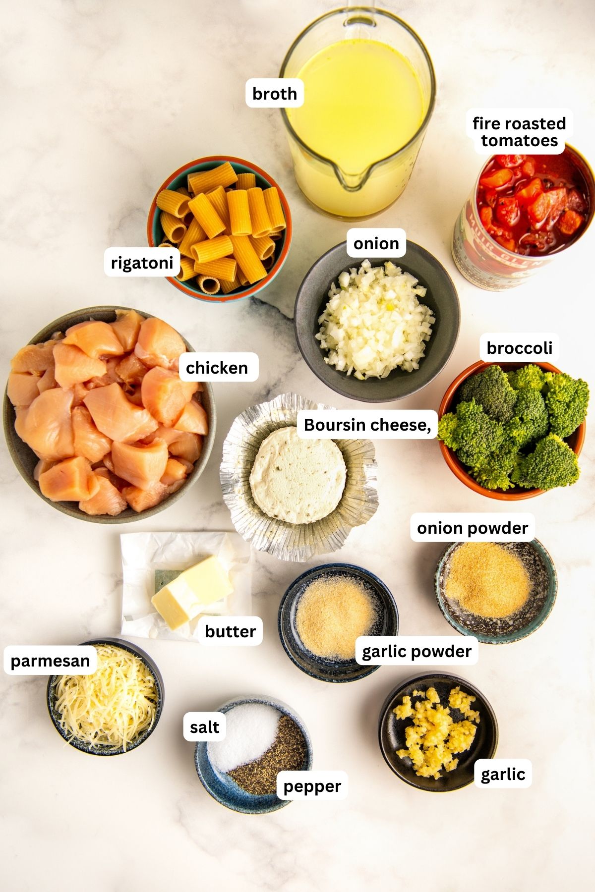 Ingredients in bowls for Boursin cheese pasta recipe. From top to bottom: chicken broth, fire roasted tomatoes, rigatoni, onion, chicken, boursin cheese, broccoli florets, butter, garlic powder, onion powder, parmesan cheese, salt, pepper and fresh garlic.