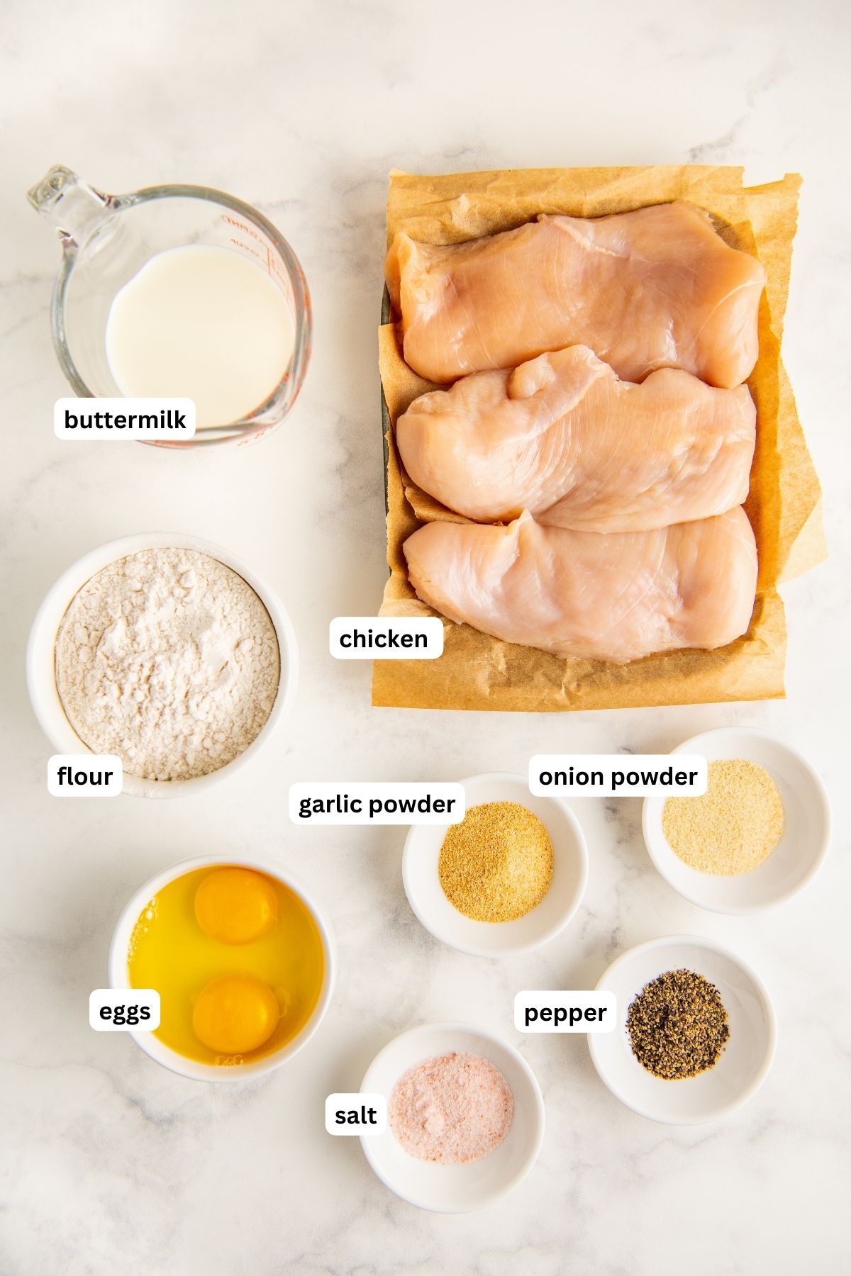 Ingredients for fried chicken for chicken and waffles recipe arranged in bowls. From top to bottom: buttermilk, chicken breasts, flour, onion powder, garlic powder, eggs, salt and pepper.