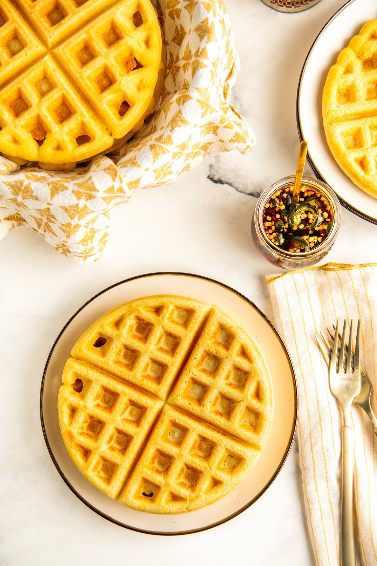 Warm cornbread waffles stacked on plates with a bowl of hot honey on the side.