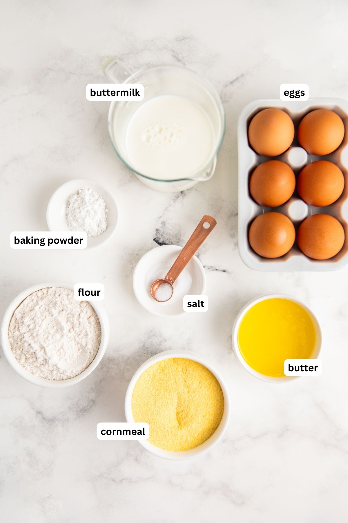 Ingredients for cornbread waffle recipe arranged in bowls, from top to bottom: buttermilk, eggs, baking powder, flour, salt, butter and cornmeal.