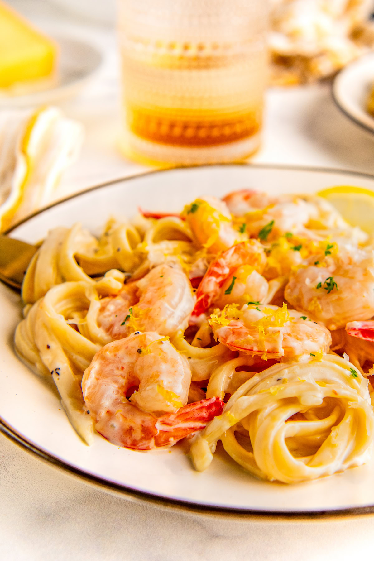 Lemon garlic shrimp pasta tossed in a parmesan cream sauce served on a plate topped with fresh lemon zest and parsley.