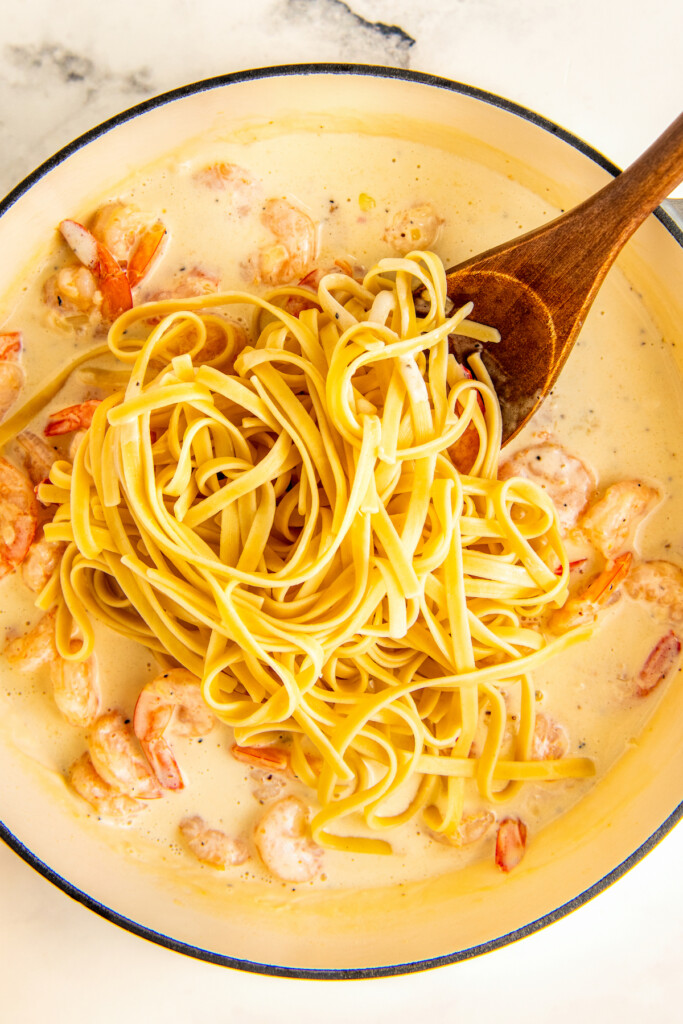 Stirring the pasta, sauce, and shrimp together. 