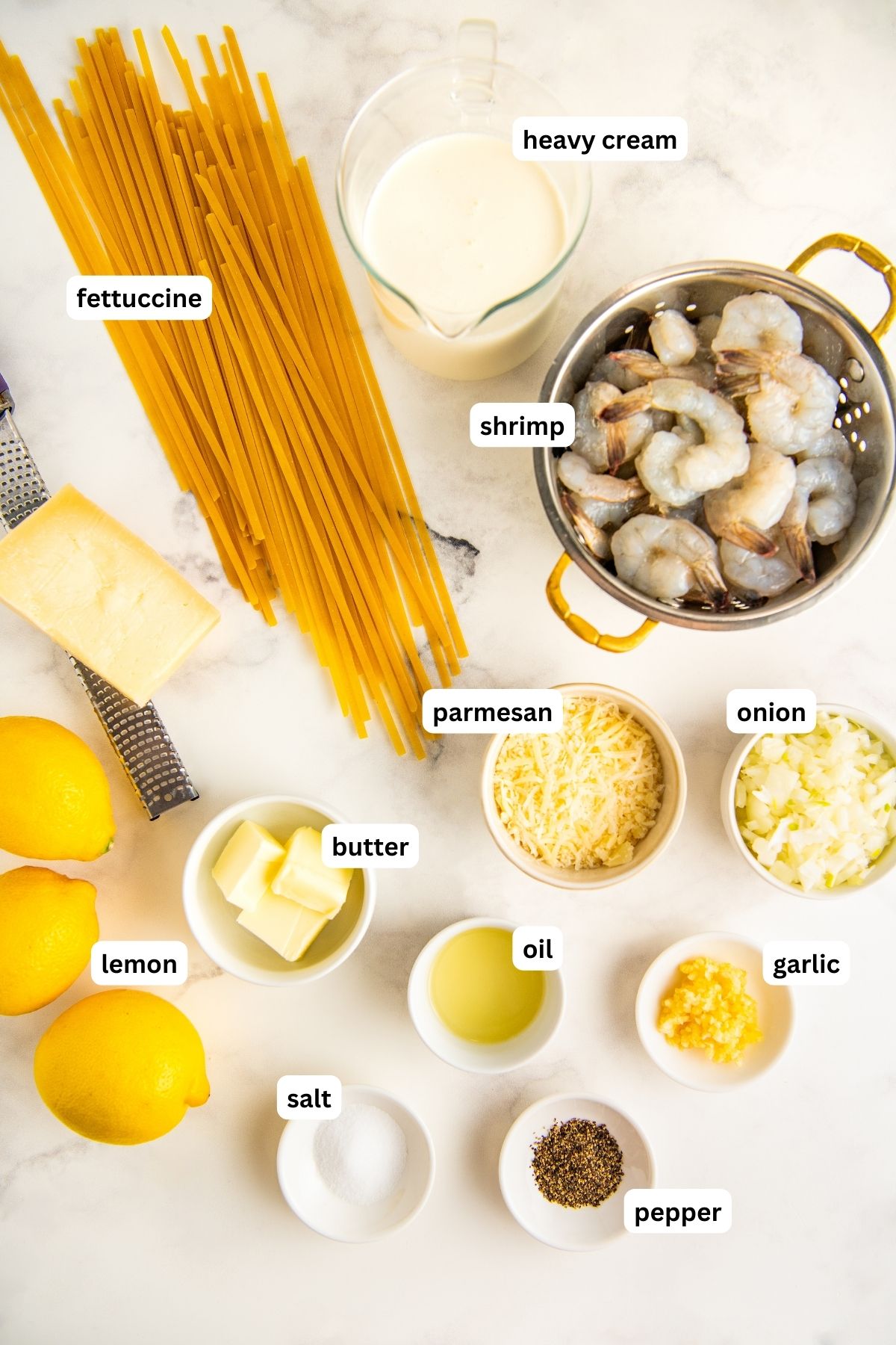 Ingredients for lemon garlic shrimp pasta recipe arranged in bowls. From top to bottom, heavy cream, fettuccine, shrimp, parmesan cheese, onion, butter, lemon, oil, garlic, salt and pepper. 