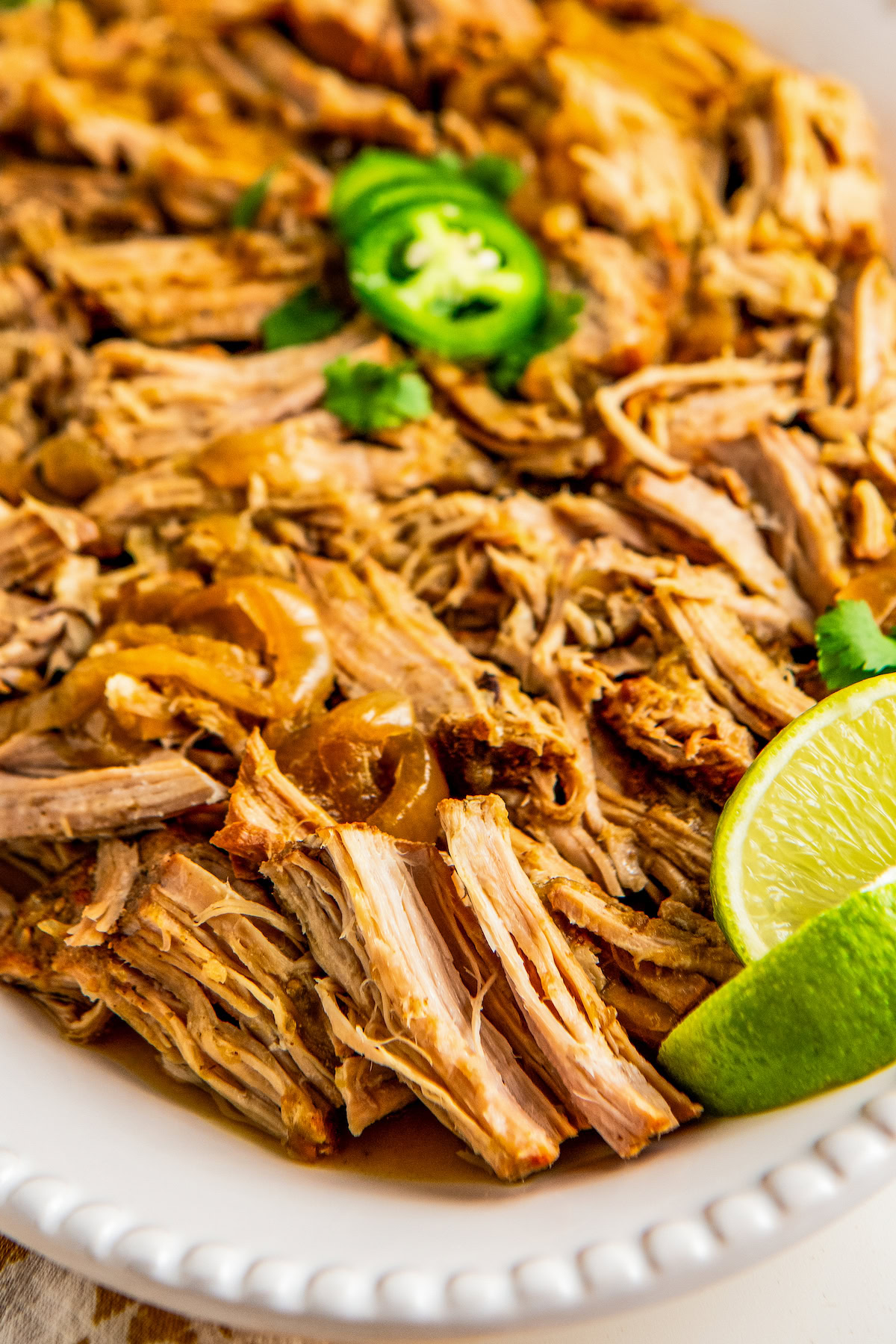 Shredded salsa verde pork with tender onions on a serving platter with a lime wedge on the side.