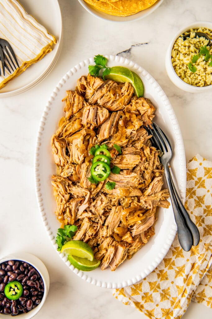 Crockpot salsa verde pork in a serving plate with sliced jalapeños on top.