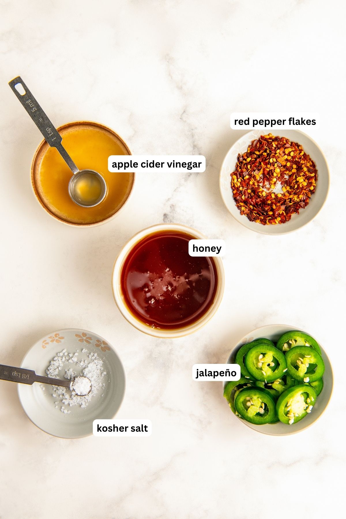 Ingredients for hot honey recipe arranged in jars. From top to bottom: apple cider vinegar, crushed red pepper flakes, honey, salt and fresh jalapeños.