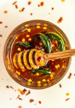 A jar of hot honey sauce with peppers in it with a honey comb dipper in the jar.
