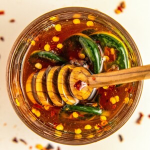 A jar of hot honey sauce with peppers in it with a honey comb dipper in the jar.